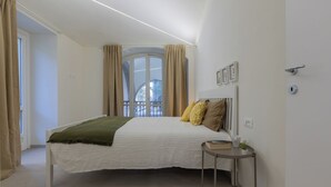 A bedroom with a bed, a bedside table, a window with curtains, and a view of the outside. - Ai Portici di Susa by Wonderful Italy (Turin)