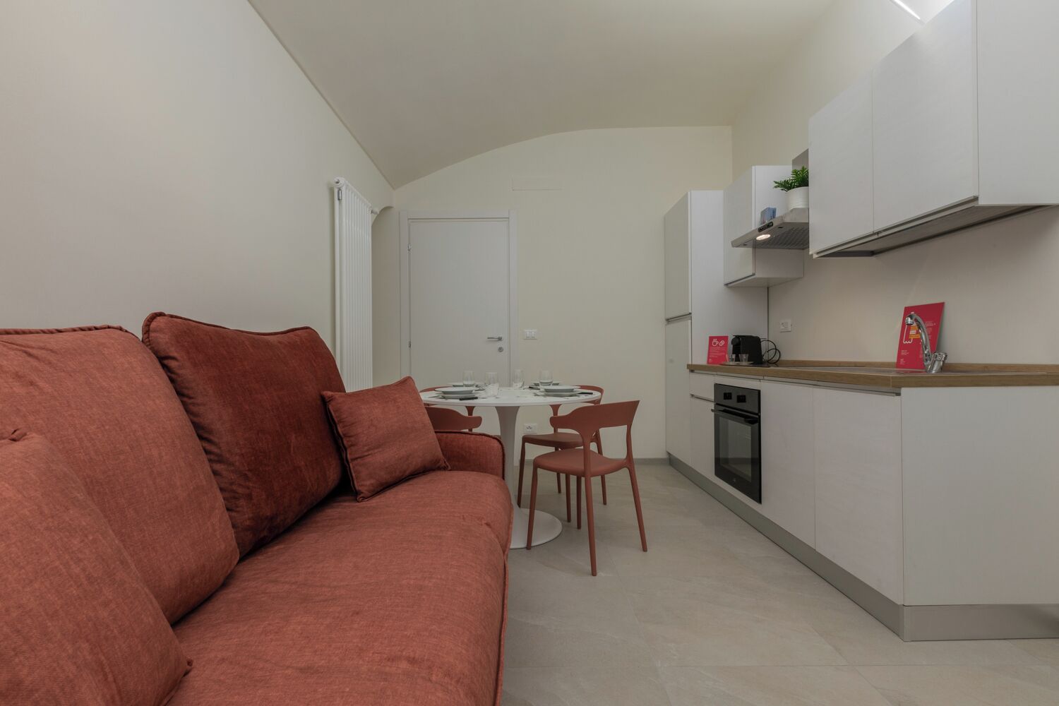 A compact living space with a sofa, dining table, chairs, a kitchenette, and a door.