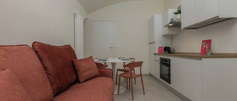 A compact living space with a sofa, dining table, chairs, a kitchenette, and a door.