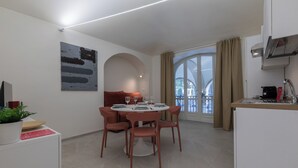 A modern dining area with a round table, red chairs, and a sofa. There is a painting on the wall, a plant, and a kitchen area with a microwave. - Ai Portici di Susa by Wonderful Italy (Turin)
