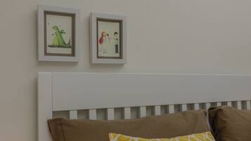 A bedroom with a white headboard, two framed pictures on the wall, and three pillows on the bed.