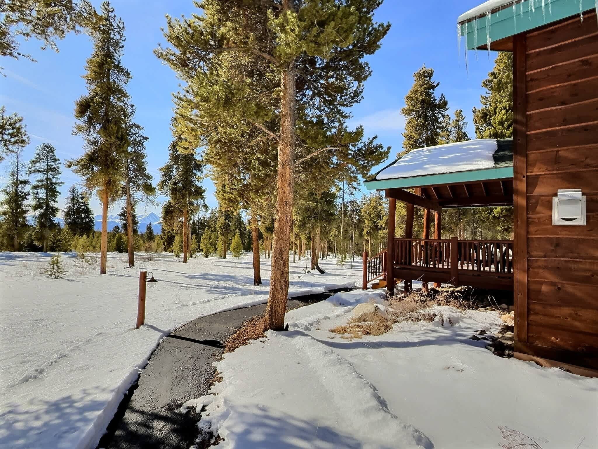 Una cabaña de madera con un porche cubierto, rodeada de nieve y altos pinos.