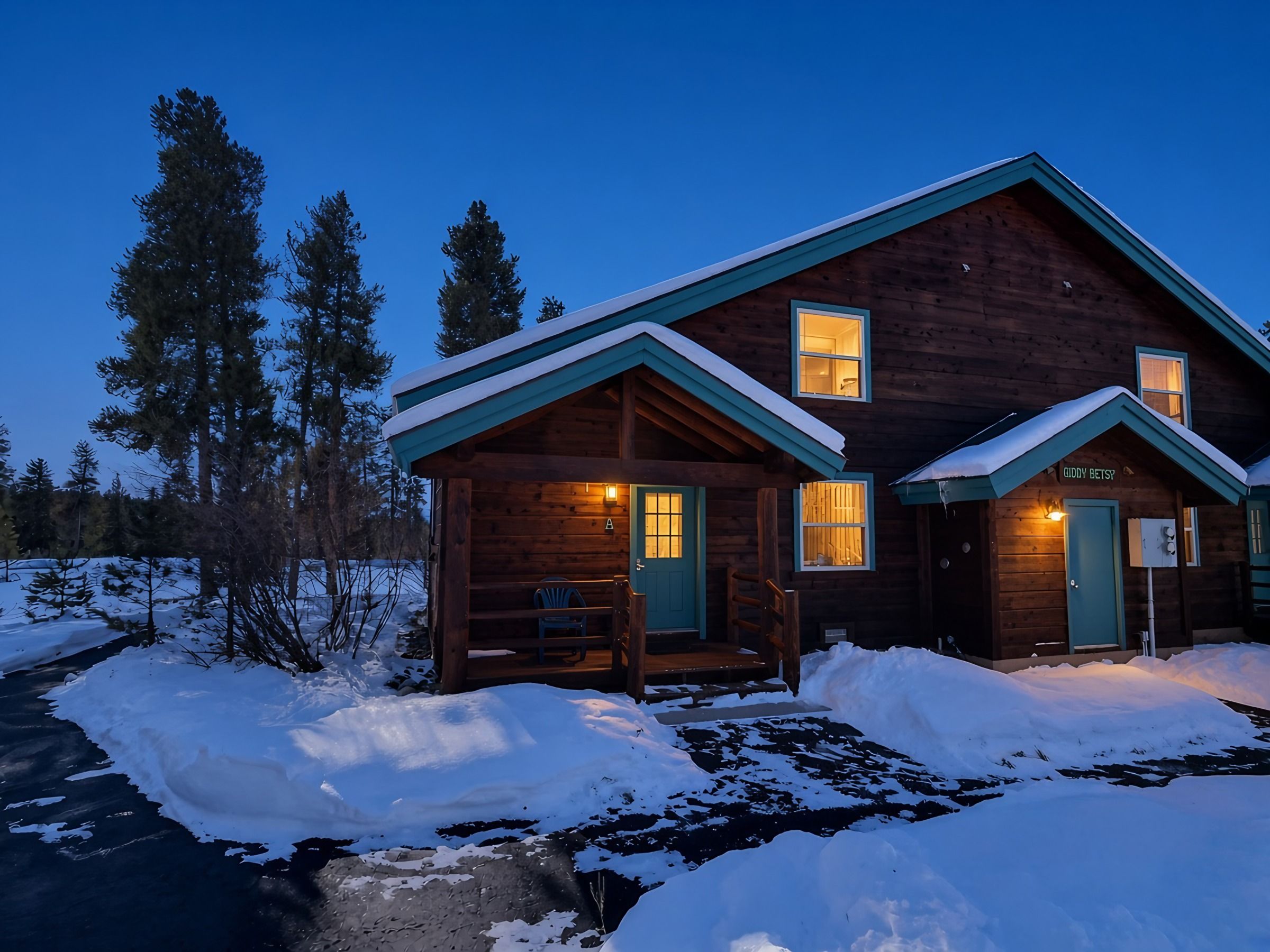 A wooden cabin with a porch and two windows, surrounded by snow.