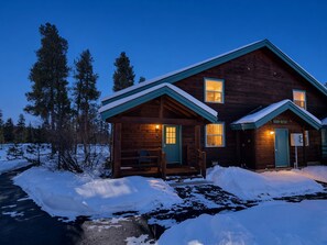 Una cabaña de madera con un porche y dos ventanas, rodeada de nieve.