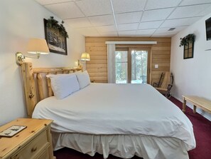 A bedroom with a wooden headboard, a bed with white bedding, a nightstand, a bench, and a window with a view of trees. - Leadville Log Cabin on 6 Acres | 3BR Sleeps 6 | Mtn Views & Fireplace (Leadville)