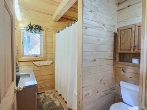 Ein Badezimmer mit Holzwänden, einem Fenster, einer Toilette und einer Duschvorhang.