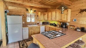 A wooden cabin-style kitchen with a refrigerator, sink, microwave, and a central island with stools.