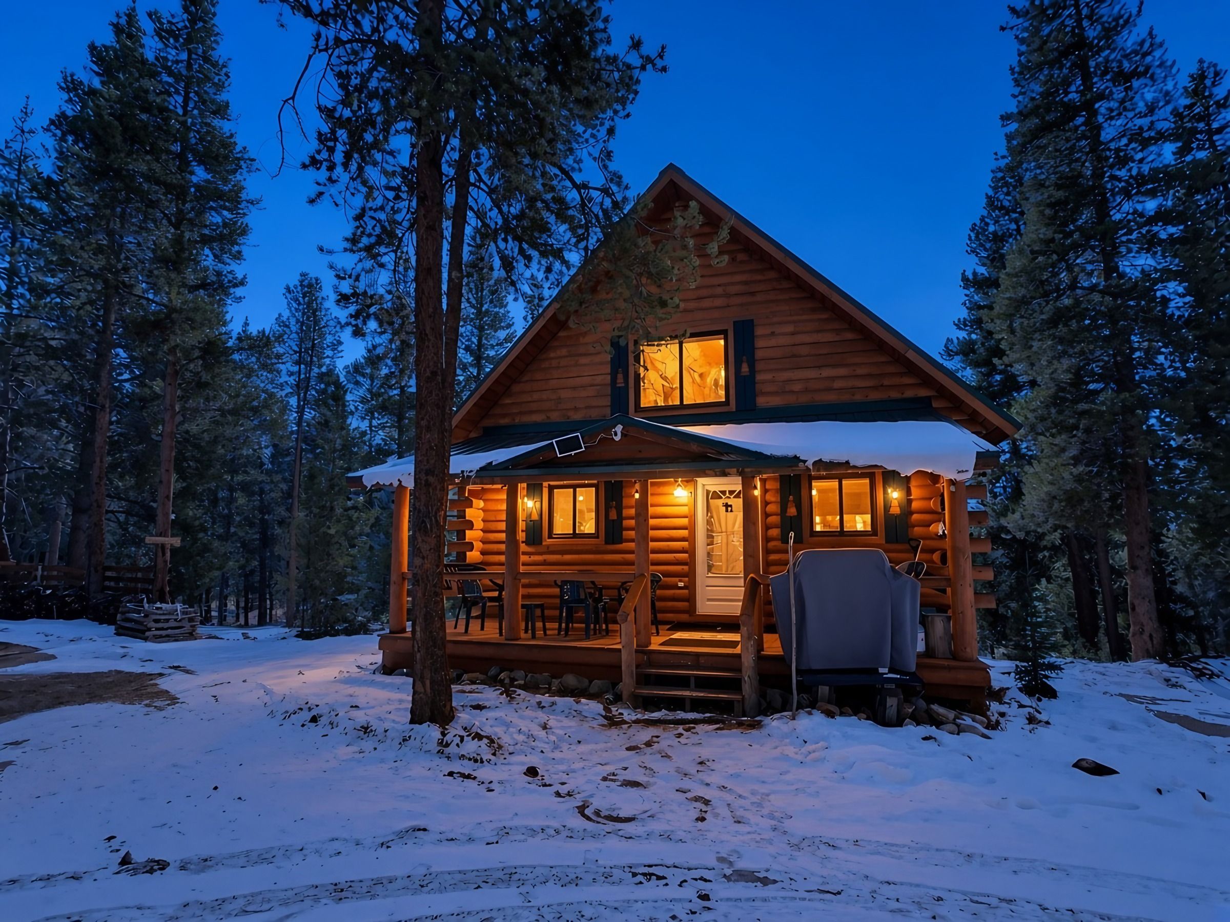 A log cabin with a porch, surrounded by snow and trees.