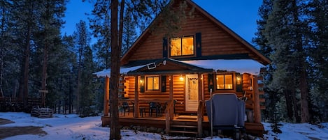 A log cabin with a porch, surrounded by snow and trees.