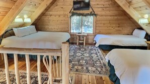 A cozy attic bedroom with two beds, a small table, and a window.