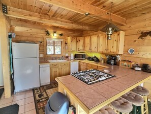 A wooden cabin-style kitchen with a refrigerator, sink, microwave, and a central island with stools. - Leadville Log Cabin on 6 Acres | 3BR Sleeps 6 | Mtn Views & Fireplace (Leadville)