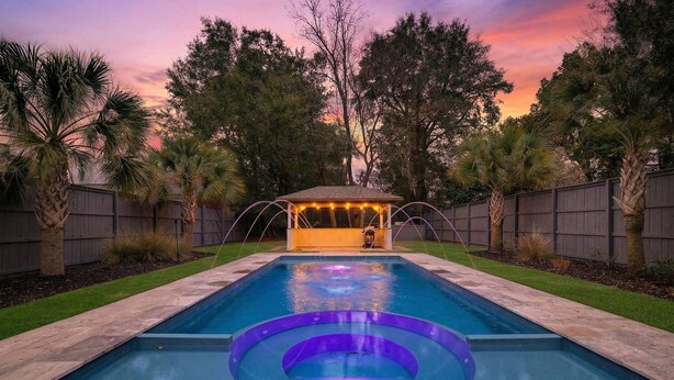 Une piscine avec un jacuzzi, entourée d’une clôture en bois et de palmiers.