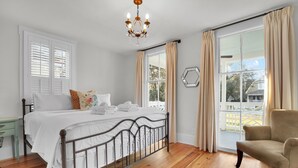 A bedroom with a bed, a chair, a chandelier, and large windows with curtains. - Incredible Coastal Getaway w/ Private Pool Near Sav + Beach by Lucky Savannah (Thunderbolt)