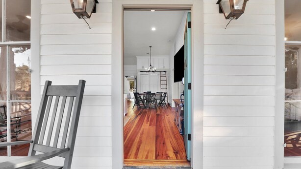 A wooden deck with a bench, a door leading to a room with a wooden floor, and two wall-mounted lanterns. - Incredible Coastal Getaway w/ Private Pool Near Sav + Beach by Lucky Savannah (Thunderbolt)