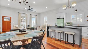 A modern kitchen with a central island, bar stools, and a dining area with a wooden table and chairs. - Incredible Coastal Getaway w/ Private Pool Near Sav + Beach by Lucky Savannah (Thunderbolt)