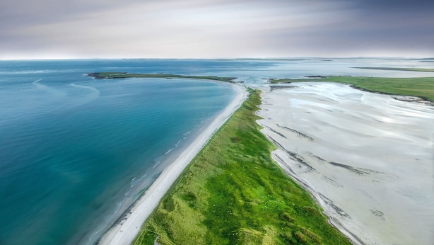 An aerial view of a coastal area with a sandy beach and green vegetation. - Orkney Retreats Kilnbarn 5* Scandi Deluxe Seafront Cottage (Kilnbarn)