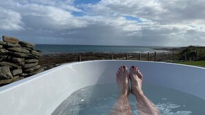A bathtub with a view of the sea and a stone wall. - Orkney Retreats Kilnbarn 5* Scandi Deluxe Seafront Cottage (Kilnbarn)