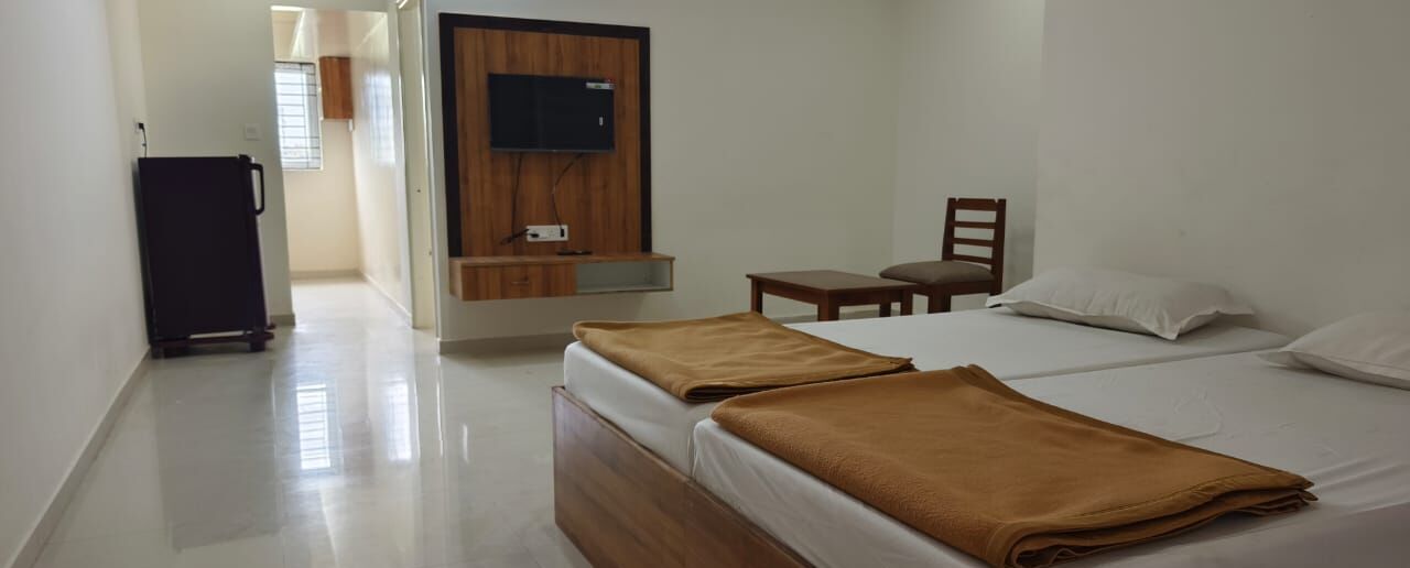 A hotel room with two beds, a TV mounted on the wall, a small table, and a chair.