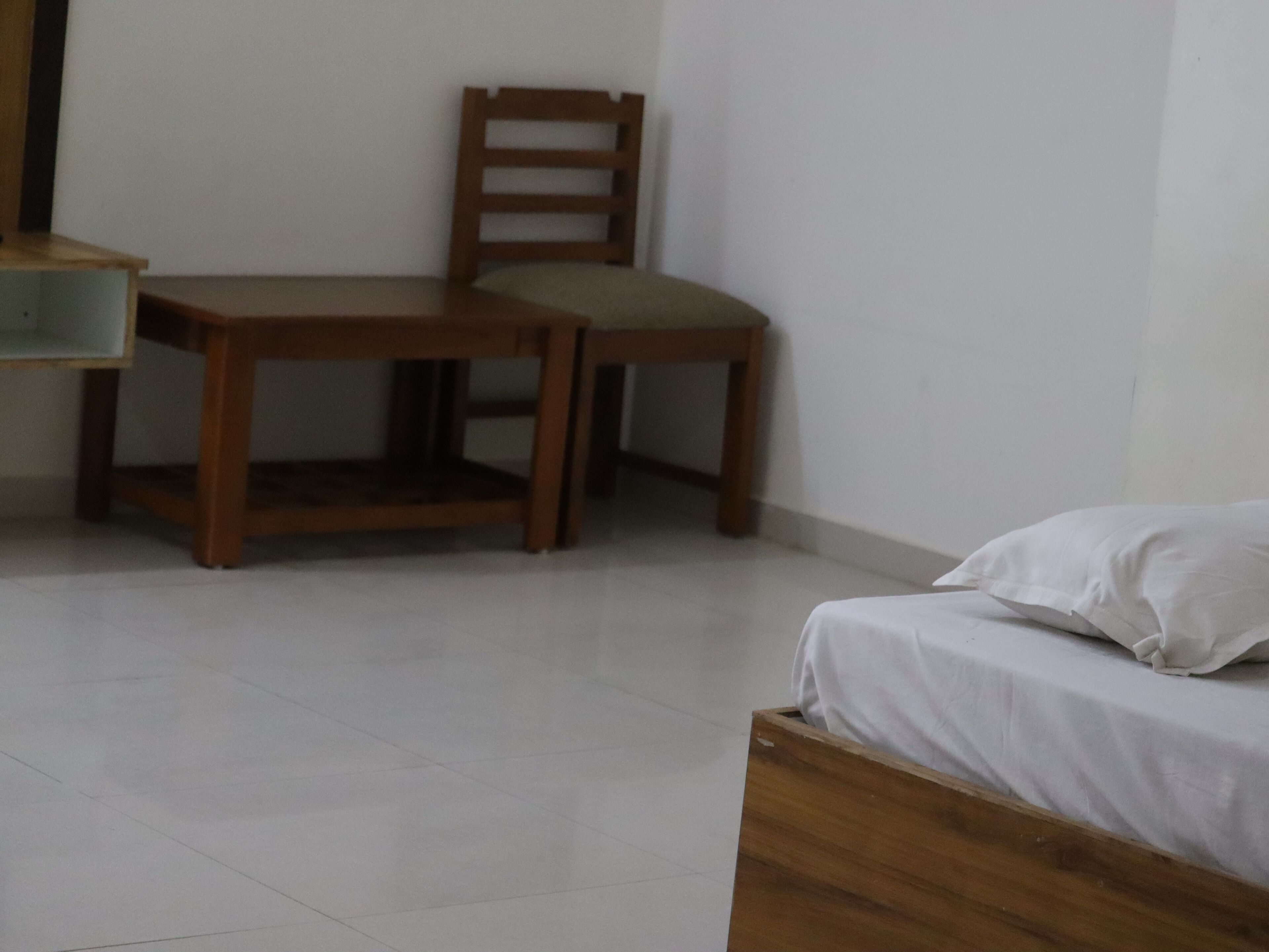 A room with a wooden desk, a chair, and a bed with white bedding.