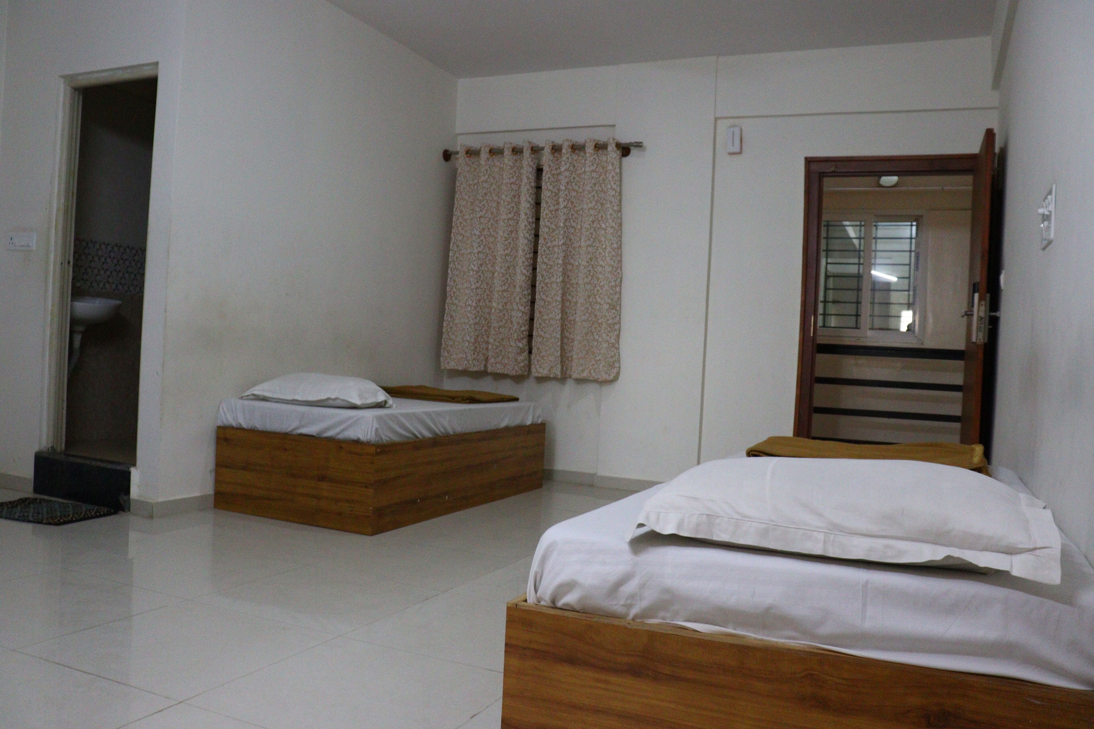 A bedroom with two beds, a wooden headboard, a small bedside table, and a window with curtains.