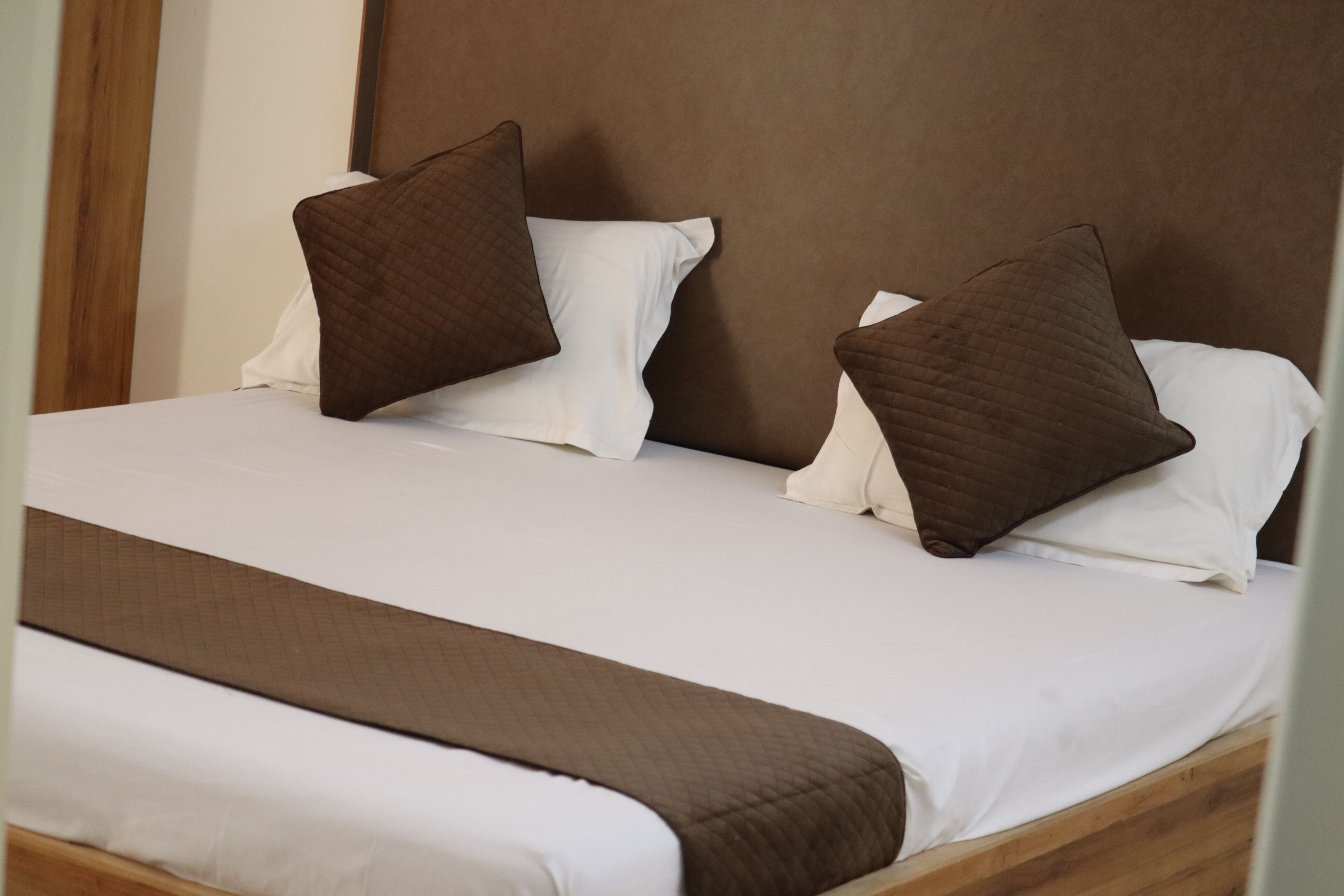 Un lit bien fait, avec une literie blanche et marron, une tête de lit en bois et un couvre-lit matelassé marron.