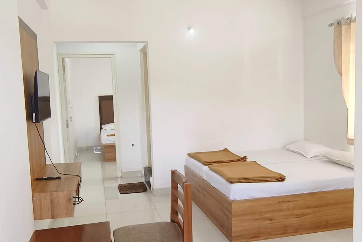 A hotel room with a bed, a desk, a chair, a television, and a door leading to another room.