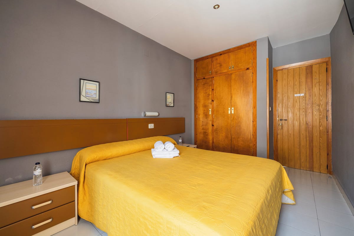 A bedroom with a bed, wooden wardrobe, and a nightstand.
