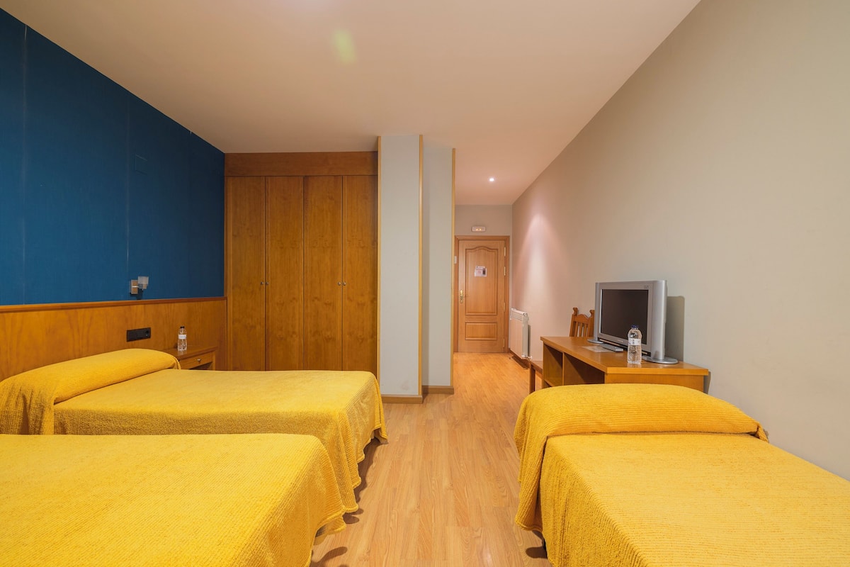 A hotel room with two beds, wooden headboards, a television, and a wooden desk.