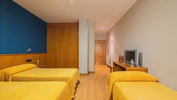 A hotel room with two beds, wooden headboards, a television, and a wooden desk.