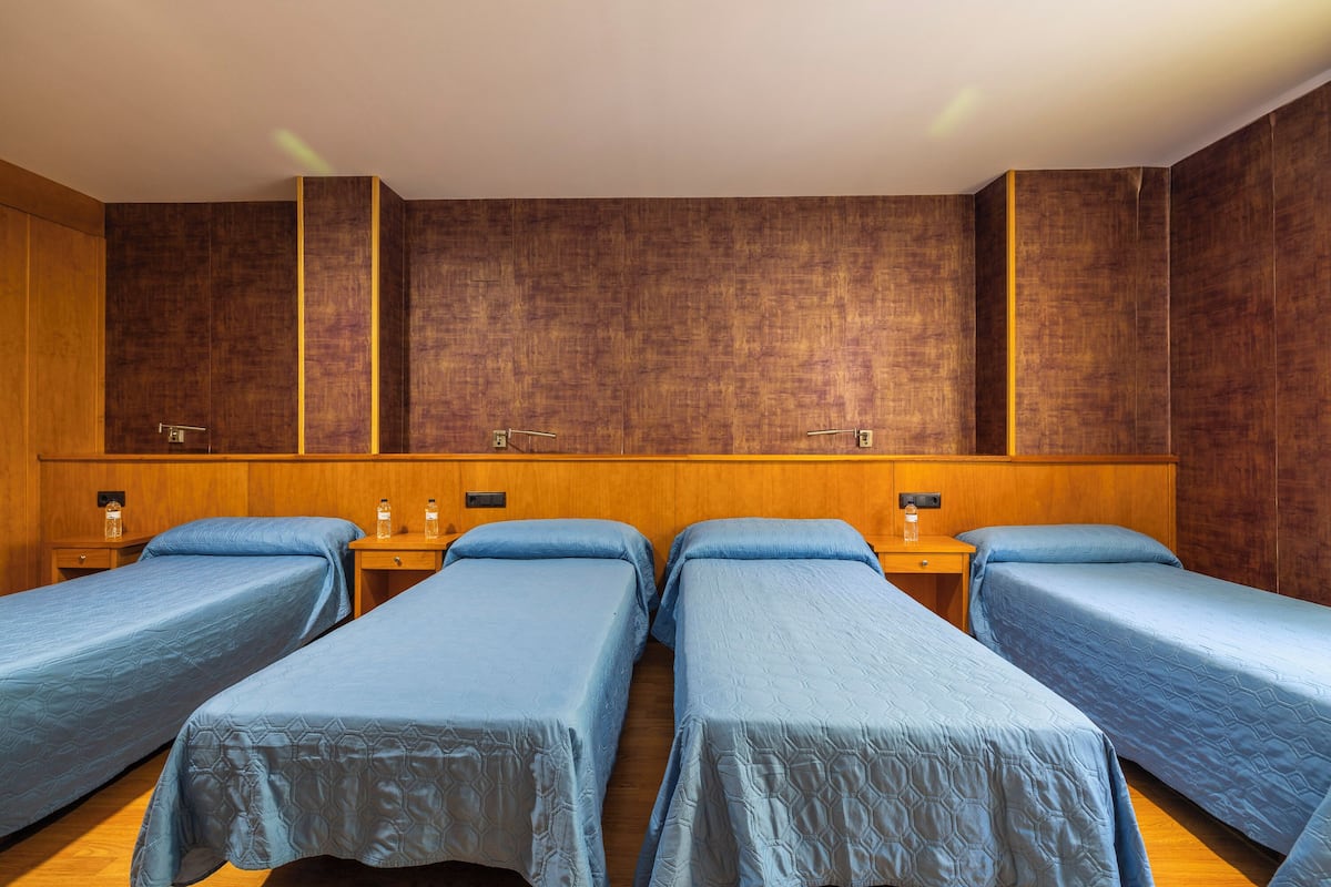 A hotel room with four single beds, wooden headboards, and a large mirror above the beds.