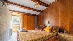 A bedroom with a large bed, wooden walls, a window, and a wooden dresser. - HOSTAL LOS VALLES  (Bielsa)