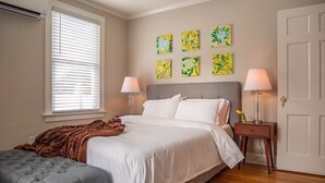 A bedroom with a bed, bedside tables, a bench, and artwork on the wall.