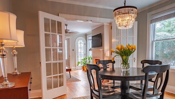 A dining area with a round table, chairs, a chandelier, and a vase with flowers.