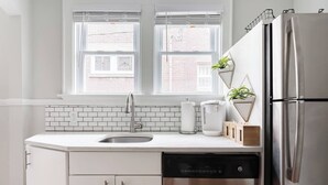A modern kitchen with a stainless steel refrigerator, a dishwasher, a sink, and a window with a view of the outside.