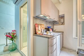 A modern kitchen with a built-in oven, a coffee machine, and a microwave. There is a window with curtains and a vase with flowers on the counter. - Maison La Vanda - Centro Citta (Sanremo)