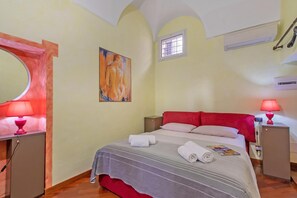 Habitación de hotel con cama, dos lámparas de noche, un pequeño armario y un cuadro en la pared, además de una ventana.