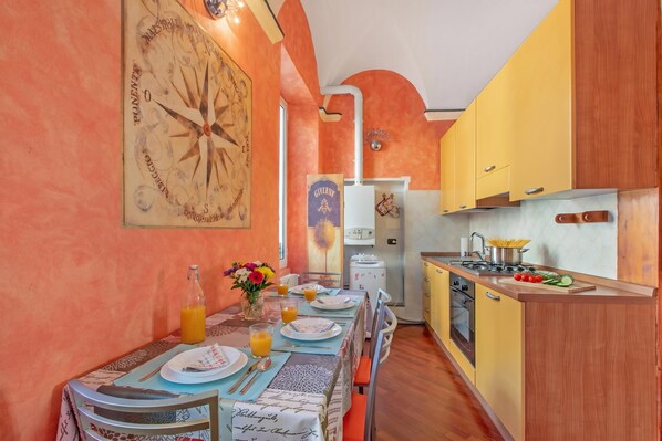Un comedor con una mesa preparada para dos, un reloj en la pared y una cocina con armarios amarillos.