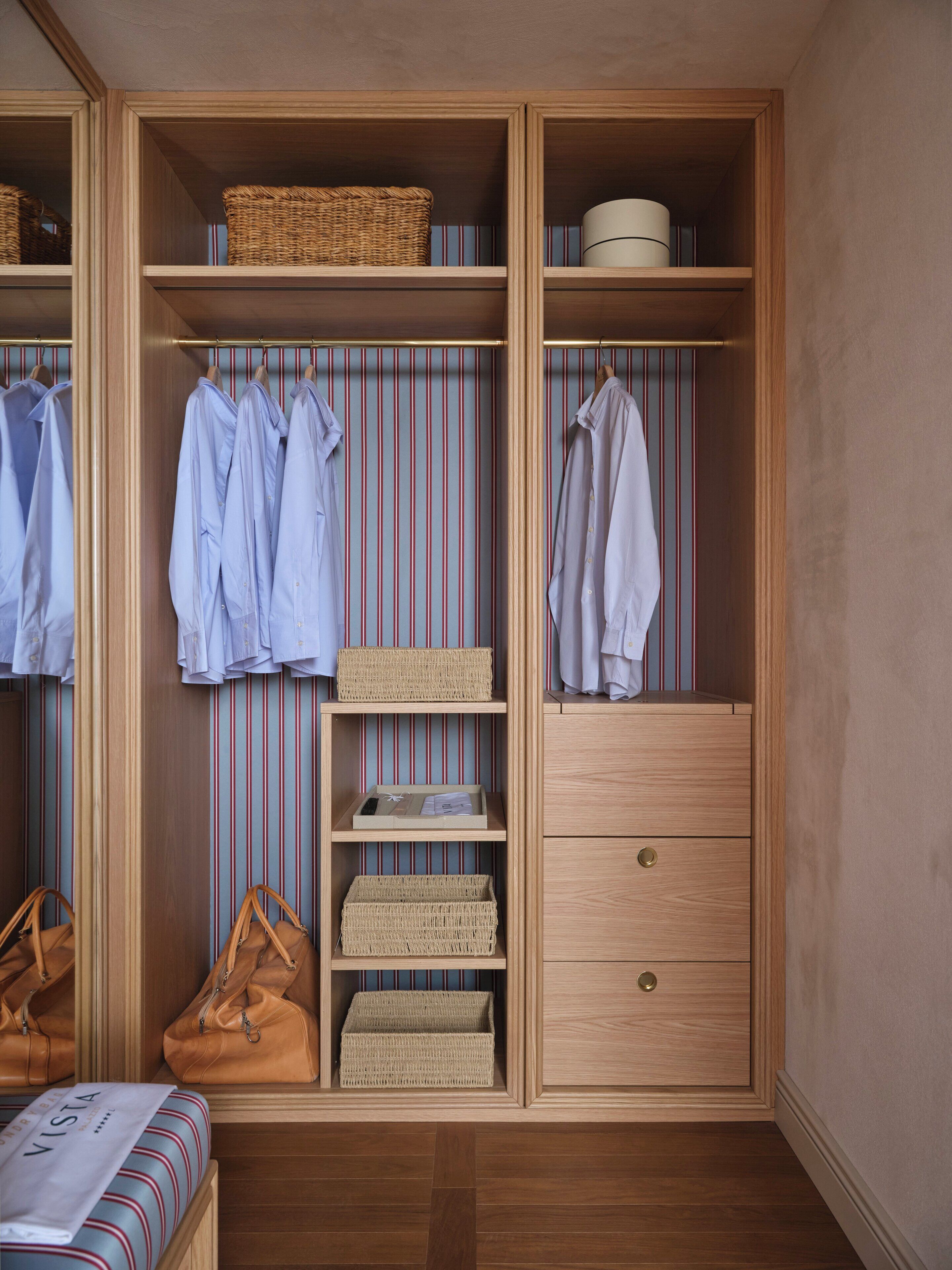 A walk-in closet with wooden shelving, hanging clothes, and storage boxes.