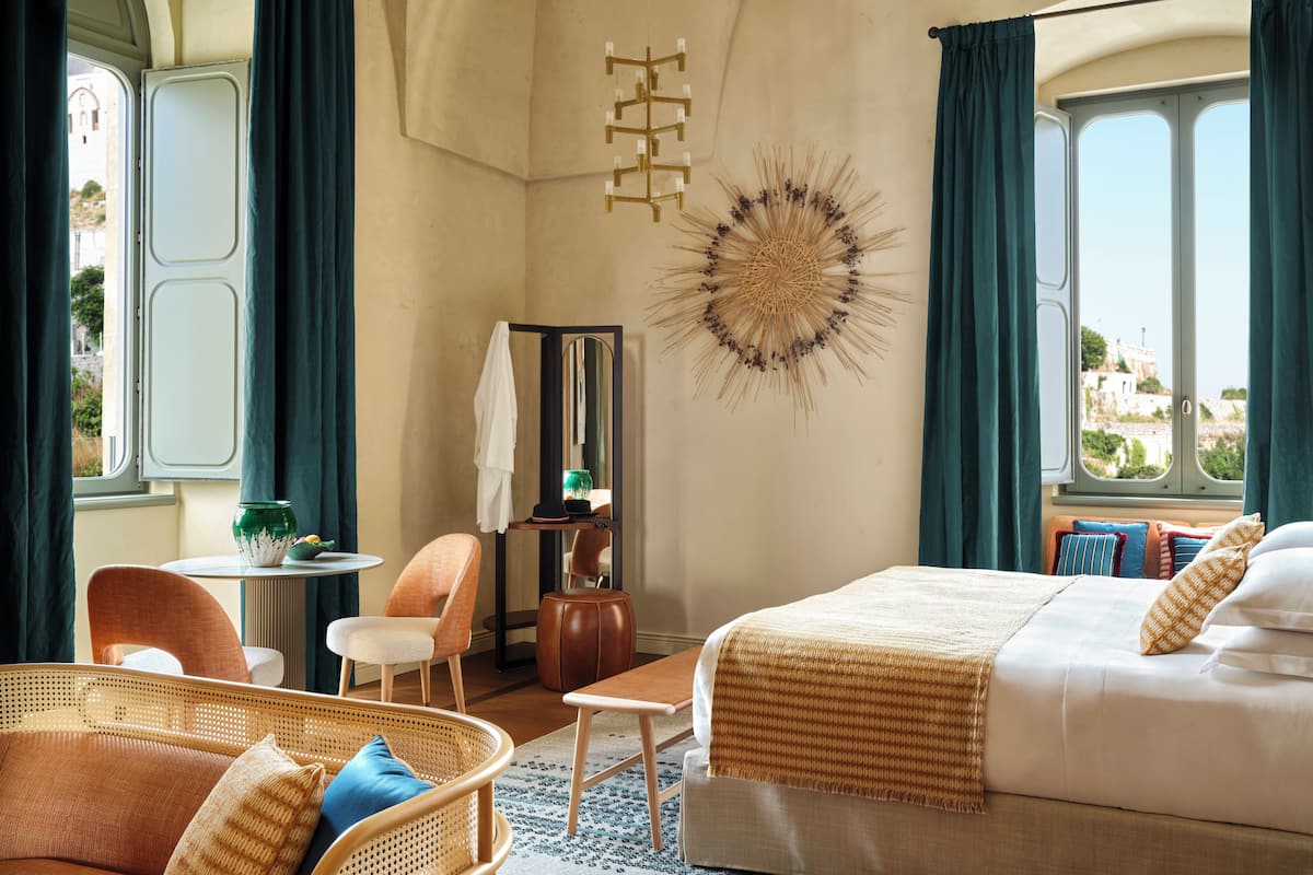 A hotel room with a bed, a chair, a small table, and a mirror.