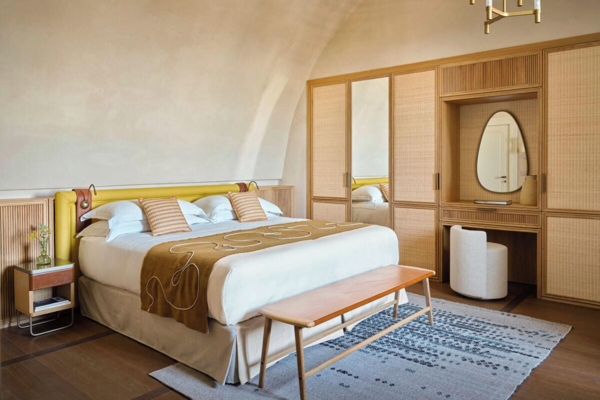 Une chambre spacieuse avec un grand lit, des tables de chevet, un banc, une armoire et un miroir.