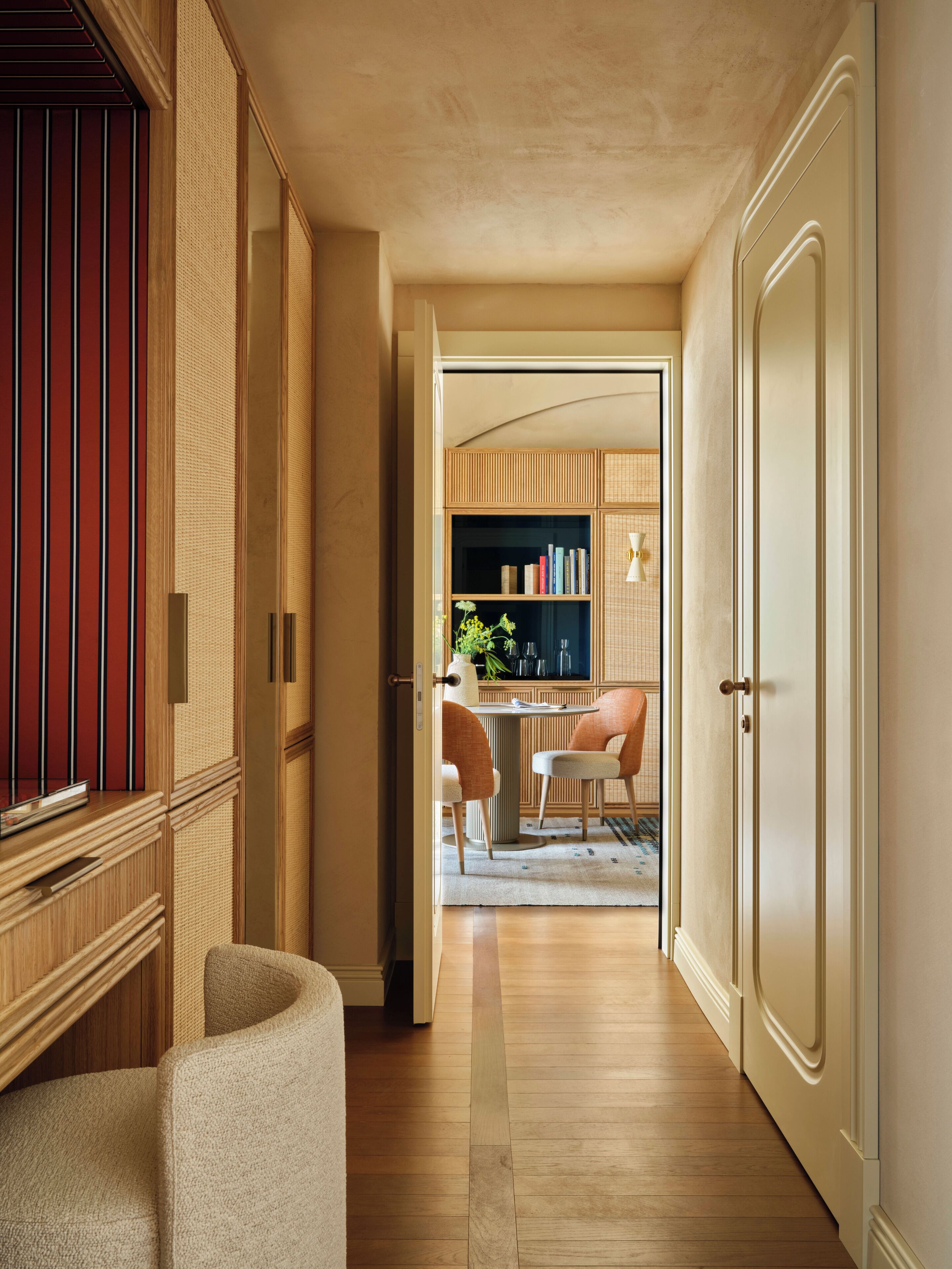 A hallway with a wooden floor, a dining area with a table and chairs, and a kitchen area with cabinets and a sink.