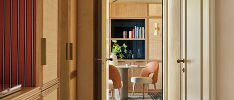 A hallway with a wooden floor, a dining area with a table and chairs, and a kitchen area with cabinets and a sink.