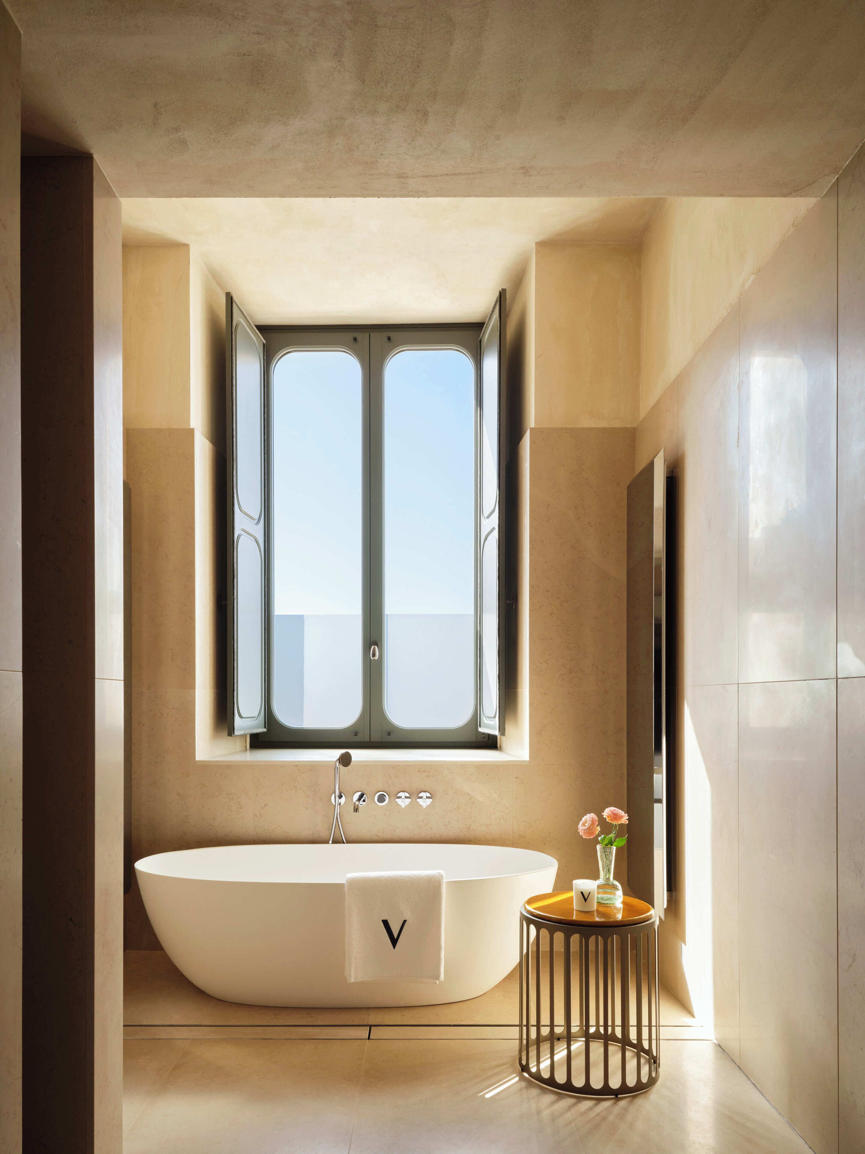 Un baño moderno con una bañera independiente, un ventanal y una pequeña mesita con flores.