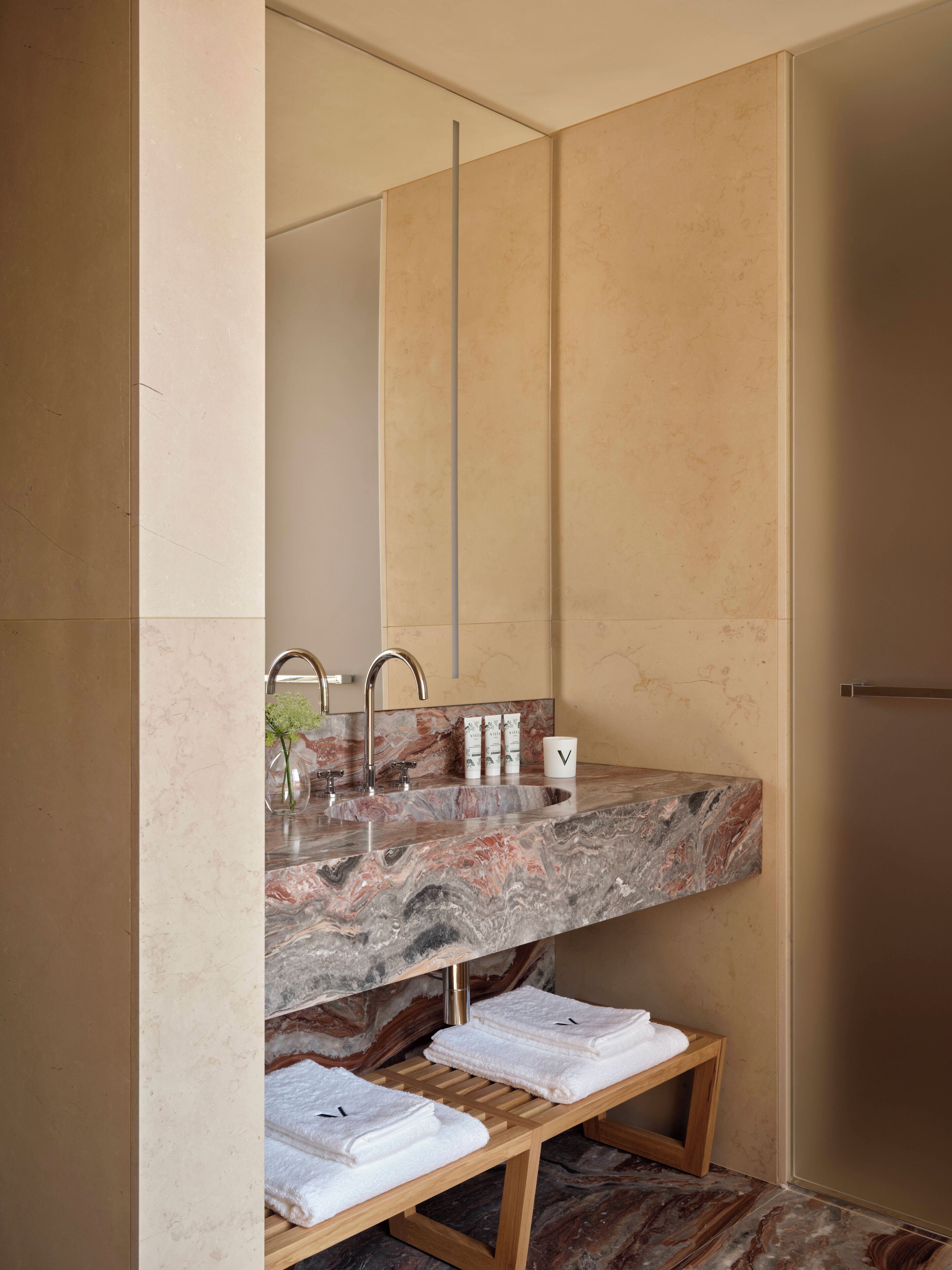 Un bagno moderno con un lavandino in marmo, uno specchio grande e una panca di legno con asciugamani.