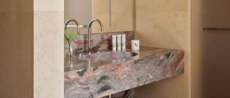 A modern bathroom with a marble sink, a large mirror, and a wooden bench with towels.