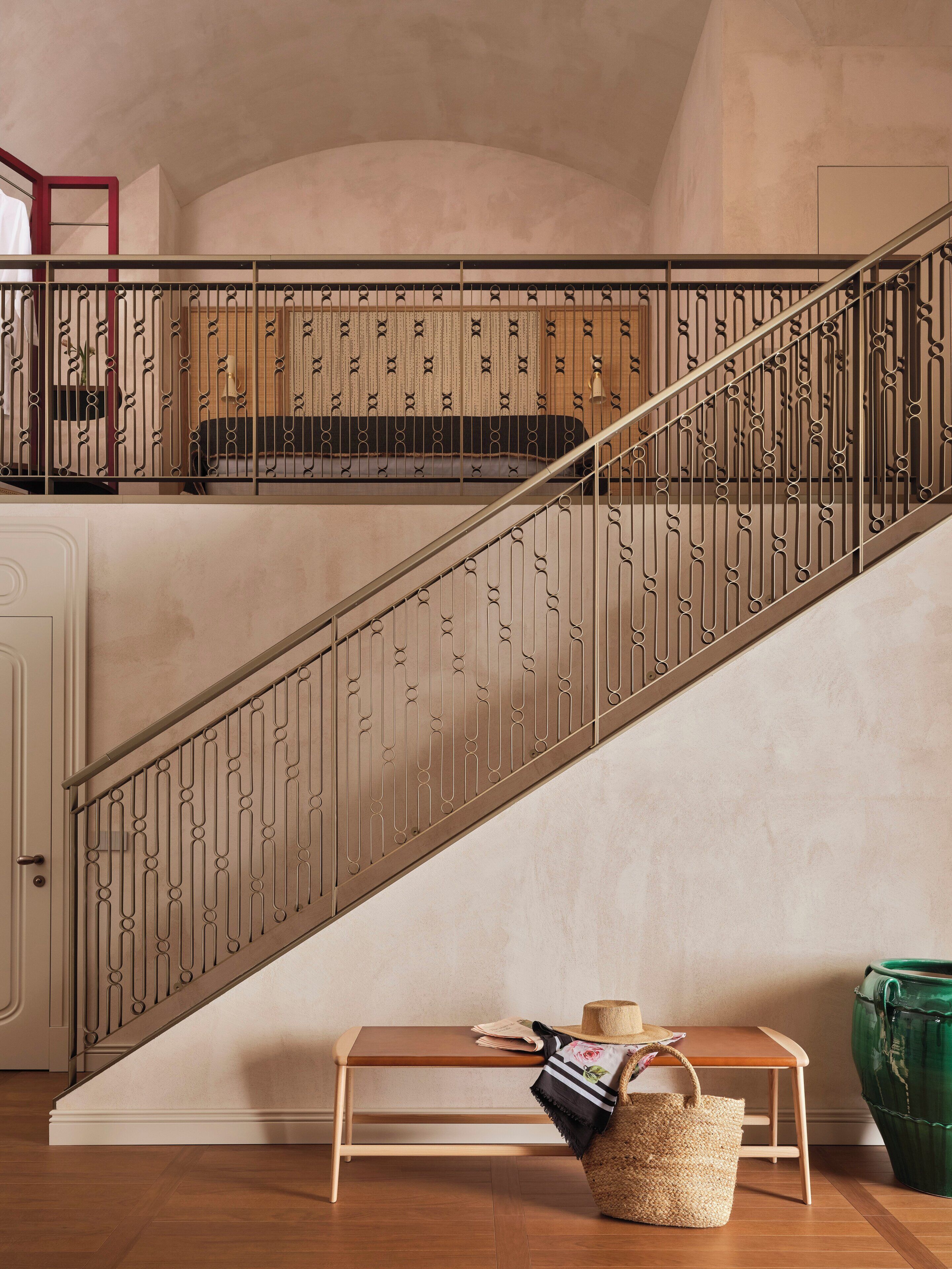 Una escalera con barandilla metálica, un banco de madera, una cesta tejida y una maceta verde.