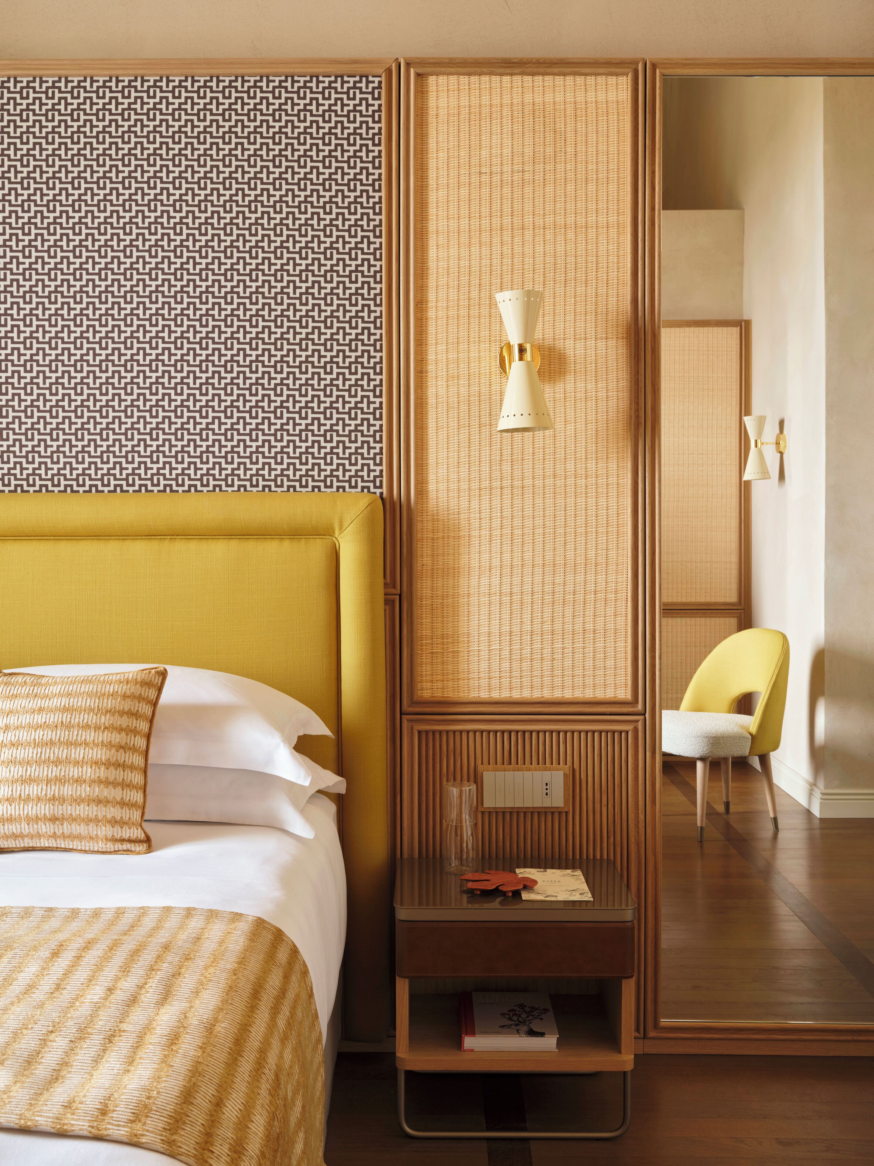 A hotel room with a bed, a nightstand, a mirror, and a chair.