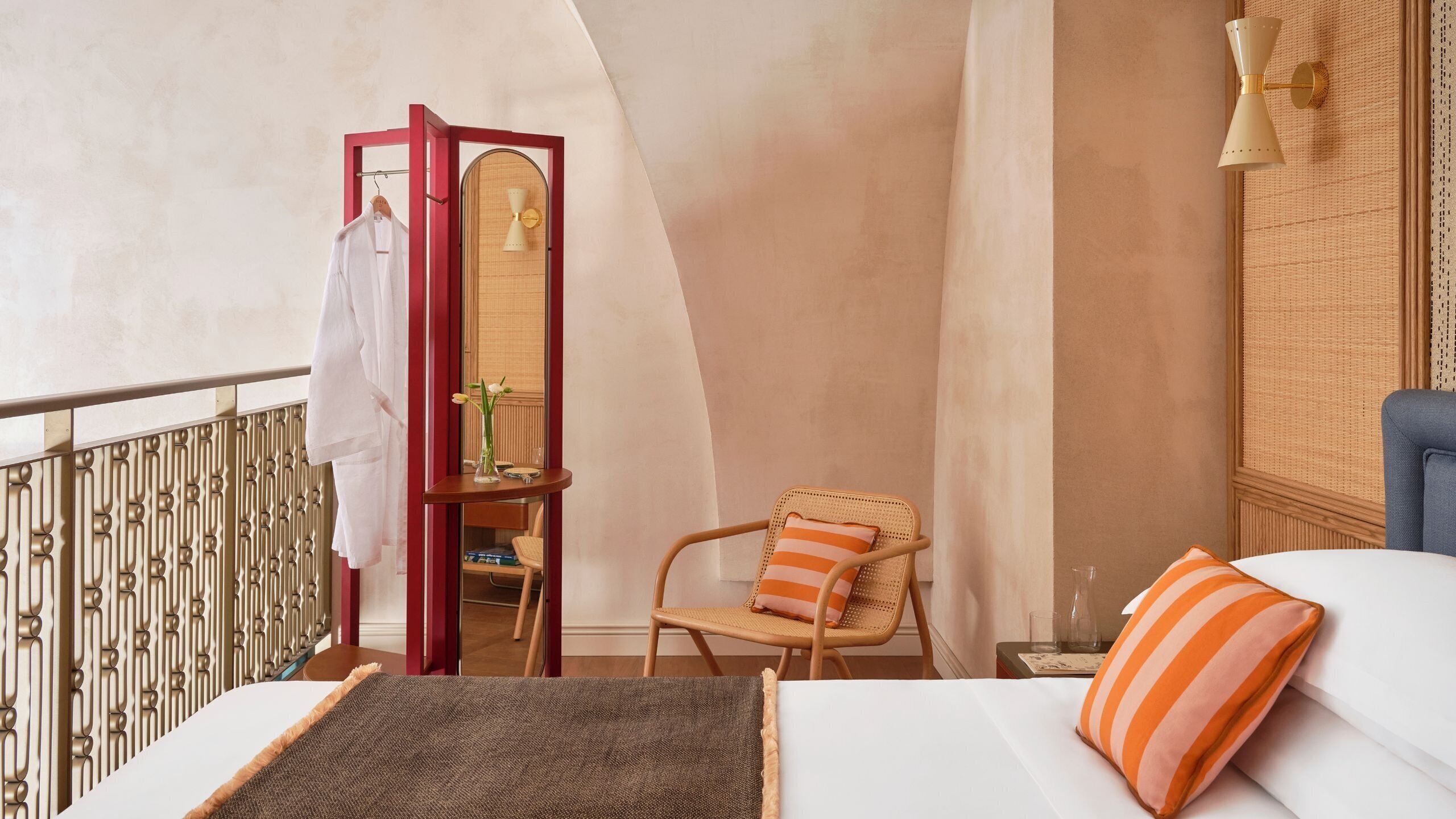 A hotel room with a bed, a chair, a small table, a mirror, and a red wardrobe.