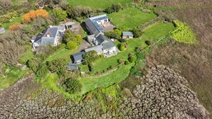 An aerial view of a rural property with multiple houses, surrounded by green fields and a rocky area. - The Noel at Lesceave (Praa Sands)