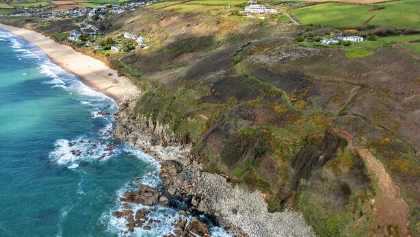 A coastal landscape with a beach, rocky cliffs, and a white building with a green roof. - The Noel at Lesceave (Praa Sands)